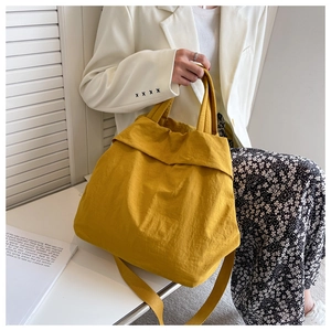 Close-up of yellow large capacity nylon tote bag held by a model in casual attire