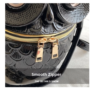 Detailed close-up of the smooth golden double zipper on a black owl-shaped crossbody bag