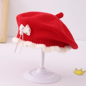 Detail of red knit beret featuring white wavy ruffle edge and cream lace bow accent