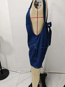 Detail view of dark blue denim jumpsuit with adjustable bow tie straps and side pocket