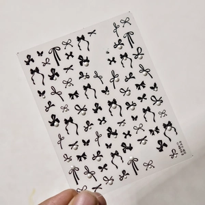 Macro detail of 3D black bow and butterfly nail stickers with white pearl accents