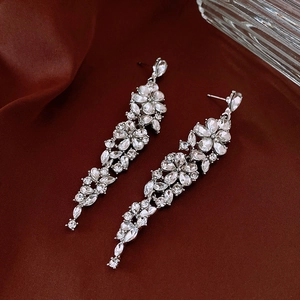 Detailed macro view of long tassel earrings with pear-cut zircons on deep red silk fabric