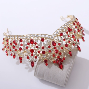 Close-up of golden bridal crown with sparkling red gems and rhinestones on beige cushion