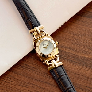 Macro detail of square gold watch case with pearl dial and black leather strap