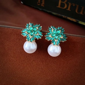 Detail view of flower-shaped green zircon earrings with white pearls on gold plating