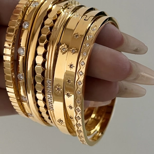 Detail of stacked gold stainless steel bangles featuring star zircon and geometric patterns
