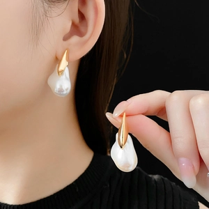 Detail of gold-plated earrings with baroque pearls worn on ear against dark background