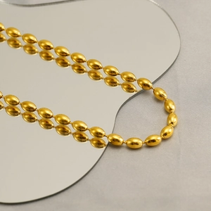 Fashionable golden stainless steel oval bead necklace shown on reflective wave mirror