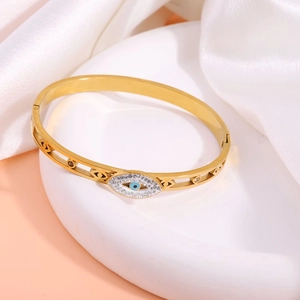 Detailed close-up of gold-plated evil eye bangle with crystals on ceramic tray