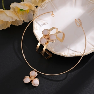 Detail eines goldenen Blumenschmuck-Sets mit rosa Emaille auf einem weißen Porzellanteller