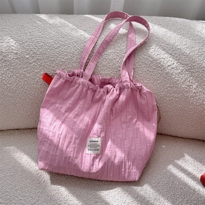 Détail du sac cabas en tissu rayé rose avec des plis doux et une étiquette carrée tissée