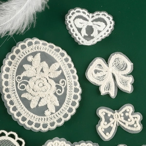 White lace embroidery patches set with floral and bow shapes on green background