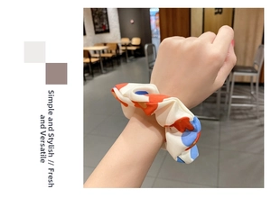 Detail of floral scrunchie in cream with blue and orange patterns worn on a wrist