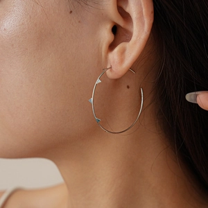 Close-up of large silver geometric hoop earring with triangular studs on a female model