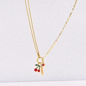 Detail of gold necklace featuring cherry charms, red gemstone, and AMOUR engraved tag