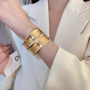 Gros plan d'un bracelet manchette doré ondulé à double couche porté par un mannequin