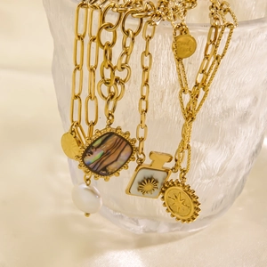 Dettaglio di collane placcate oro 14K con perle e ciondoli in conchiglia su vetro