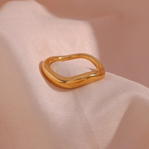 Detailed close-up of a gold irregular wavy ring on a soft pink silk fabric background
