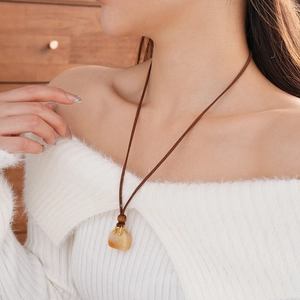 Close-up of handbag-shaped stone pendant with brown cord and golden accents necklace