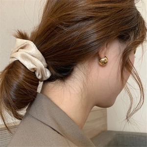 Detail view of a beige silk scrunchie and elegant gold ball stud earrings on a model