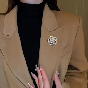 Élégante broche camélia plaquée or avec zircons et une perle blanche sur un manteau