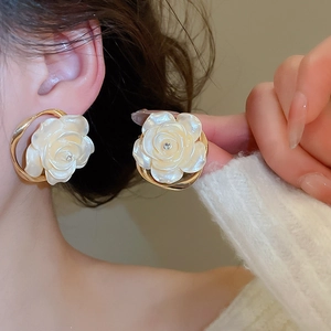 Gros plan sur les boucles d'oreilles camélia blanc avec bord doré et diamant porté