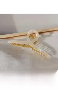 Detail of a large pearlescent resin and gold metal claw clip on white fabric