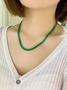 Close-up of a model wearing a luxury gold necklace with a vibrant green zircon pendant