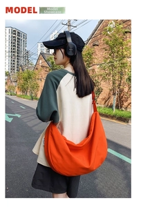 Outdoor model shot of a vibrant orange large capacity nylon half-moon crossbody bag