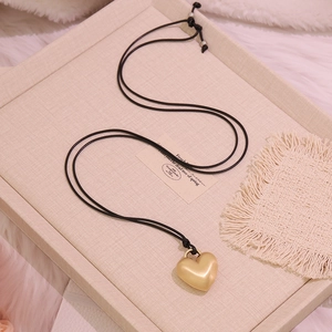 Detail of golden frosted heart pendant with black rope chain and pearl accent