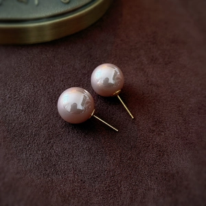 Detailed close-up of large pink-brown pearls on golden studs against velvet background
