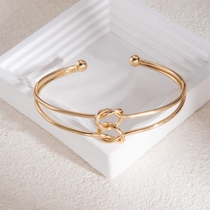 Détail d'un bracelet manchette doré à double rangée avec nœud sur support blanc