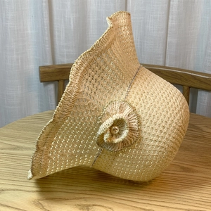 Close-up of beige woven straw sun hat with wavy brim and side flower detail with pearl