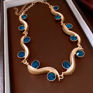 Golden wave necklace featuring deep blue round crystals on a luxury display cushion