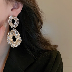 Macro detail of textured silver geometric hollow earrings worn by a model in profile
