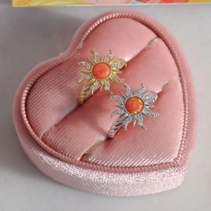 Detail of gold and silver sunburst rings with orange opal in a pink velvet box