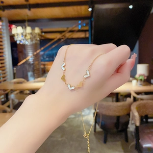 Close-up of a gold heart charm bracelet with white mother of pearl inlay on model's wrist