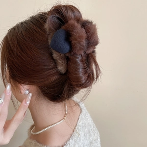 Détail d'une pince à cheveux en peluche marron avec cœur bleu sur une coiffure élégante