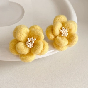 Détail macro de boucles d'oreilles fleur en résine jaune avec texture velours et perles blanches