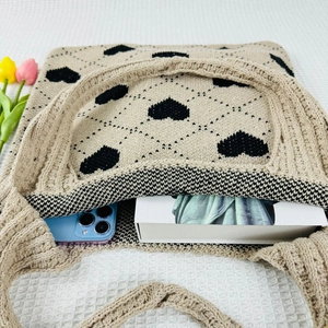 Beige knit tote bag with black heart patterns showing interior capacity with phone and book