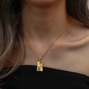 Close-up of golden rectangular pendant with sunburst texture and twisted rope chain