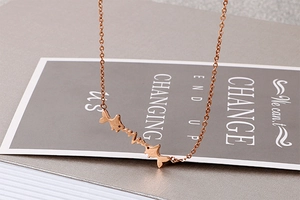 Close-up of rose gold heartbeat necklace with two small fish charms on a dark gift card