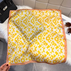 Detailed view of square silk scarf with yellow geometric patterns and pink border on plush rug