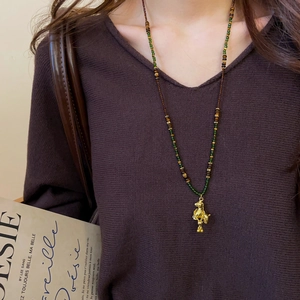 Detailed close-up of a vintage-style gold puppy pendant on a green and brown beaded chain