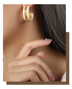 Detail of C-shaped gold-plated titanium earrings with cream enamel and hammered texture