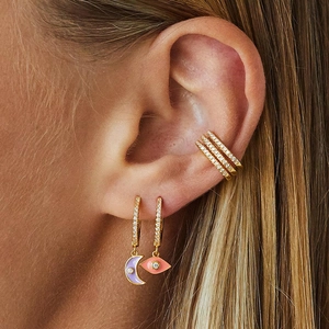 Close-up of gold moon earrings with purple enamel and sparkling rhinestone ear cuff