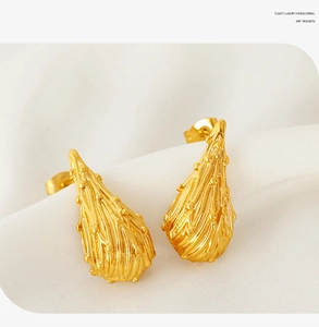 Macro view of gold water drop earrings with textured lava finish on soft white cloth