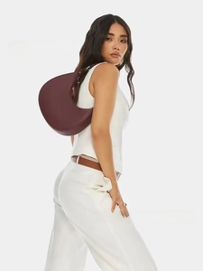 Close-up of a burgundy leather half-moon shoulder bag worn by a model in a studio