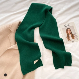 Detail of green knitted scarf with ribbed texture on cozy white bedding and beige coat