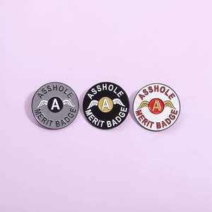 Lot de trois pin's ronds en émail avec des ailes et le texte Asshole Merit Badge en gris et noir